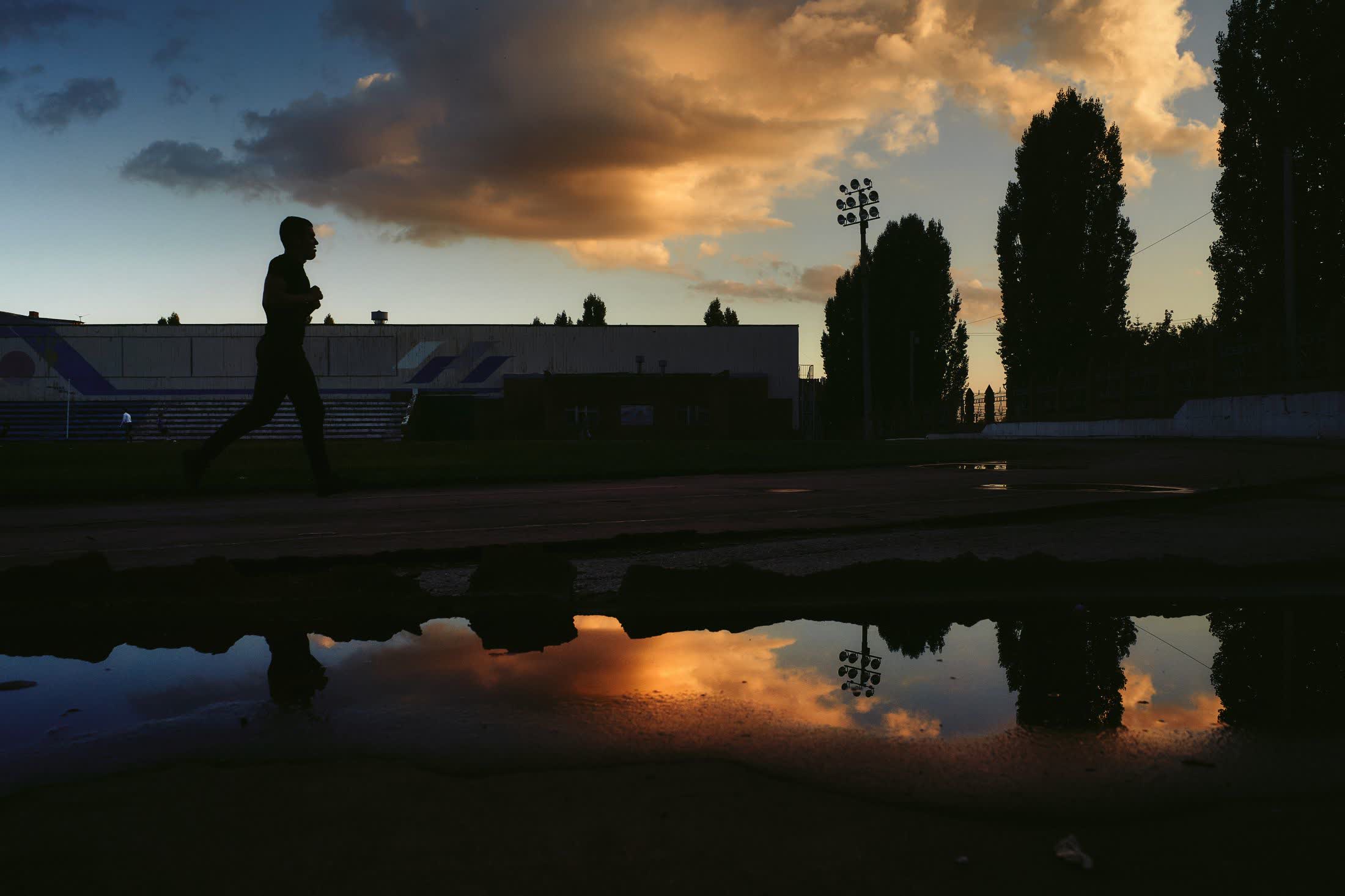 A runner silhouetted against a sunset on an empty track